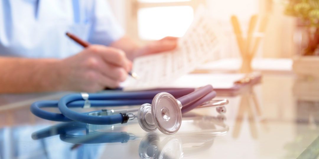 Close up of stethoscope and doctor sitting in a background filling in documentation