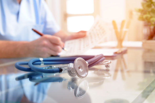 Close up of stethoscope and doctor sitting in a background filling in documentation