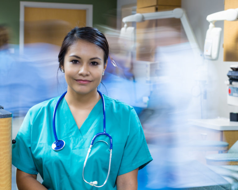 Pretty Hispanic nurse standing still in busy hospital