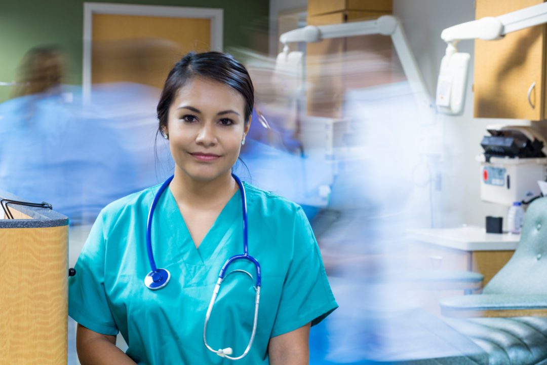 Pretty Hispanic nurse standing still in busy hospital