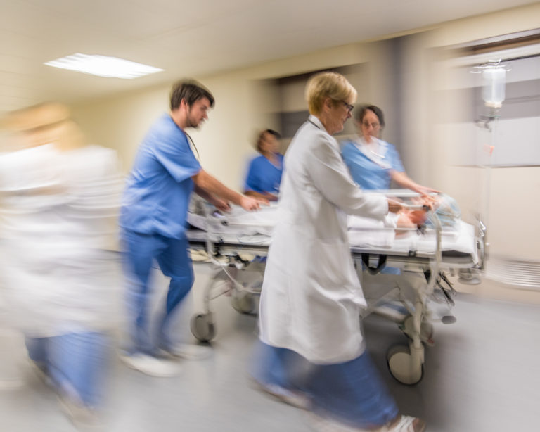 Doctors and nurse wheeling patient on stretcher in hospital's corridor.