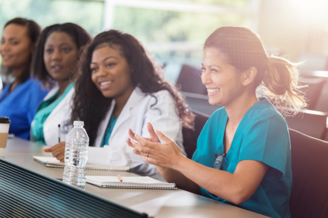 Mid adult female Asian medical professional applauds speaker at a medical conference. Her female colleagues are sitting beside her.