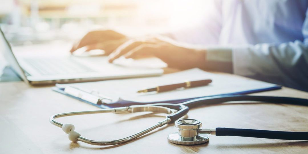 Doctor typing information on Laptop in Hospital office focus on Stethoscope