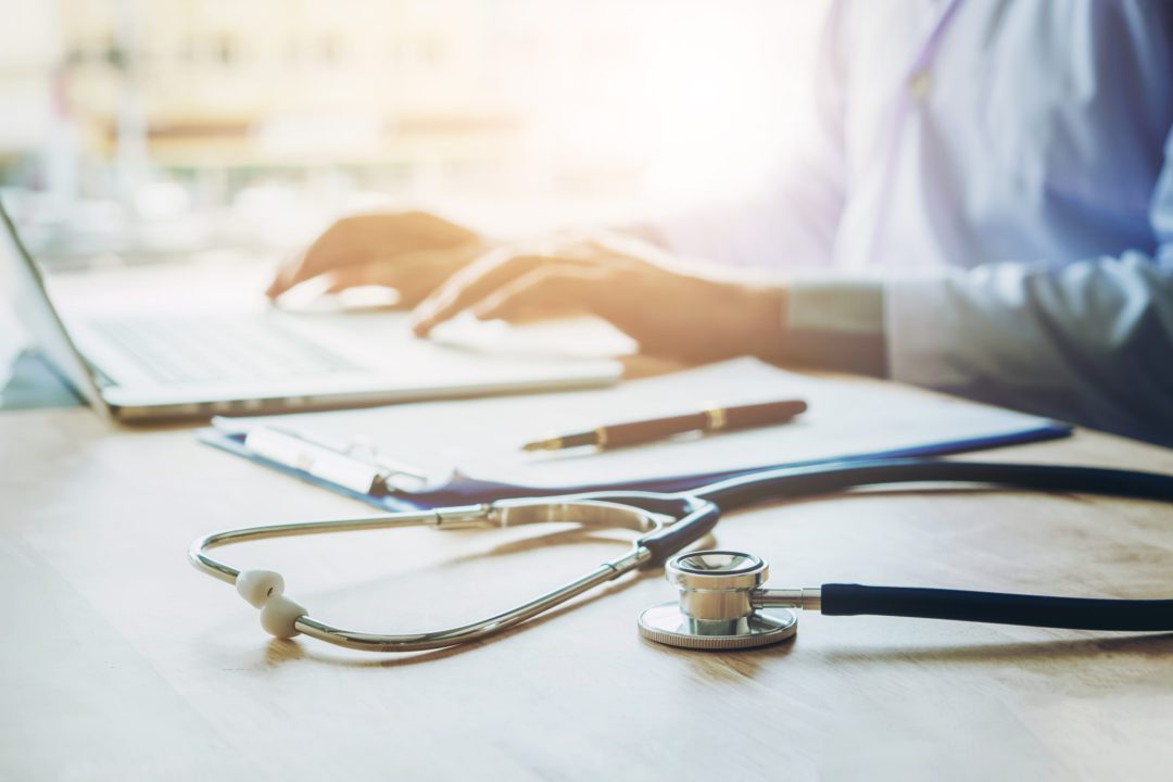 Doctor typing information on Laptop in Hospital office focus on Stethoscope