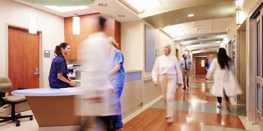 healthcare workers walk down hallway near busy nurse station