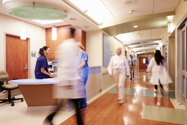 healthcare workers walk down hallway near busy nurse station