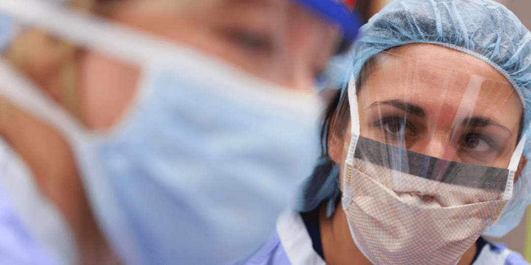 female healthcare worker in PPE looks at colleague who is blurred in the foreground