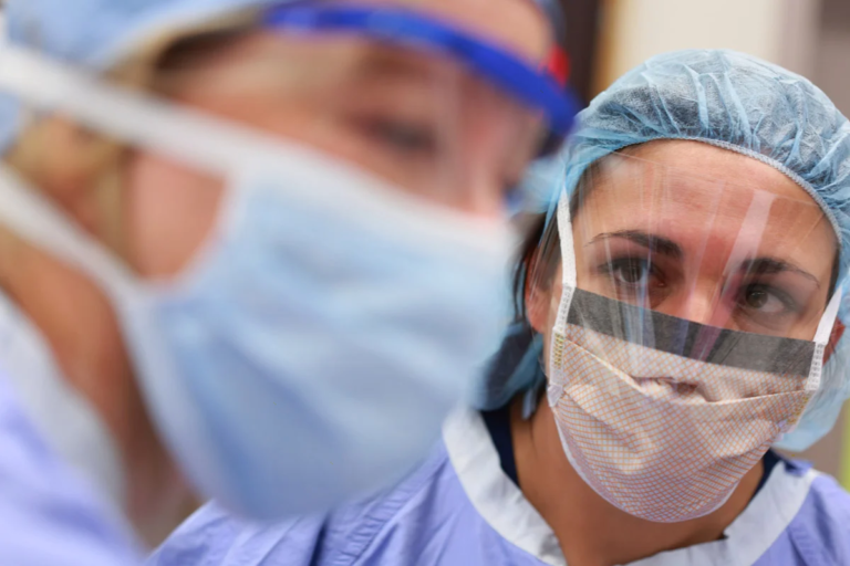 female healthcare worker in PPE looks at colleague who is blurred in the foreground