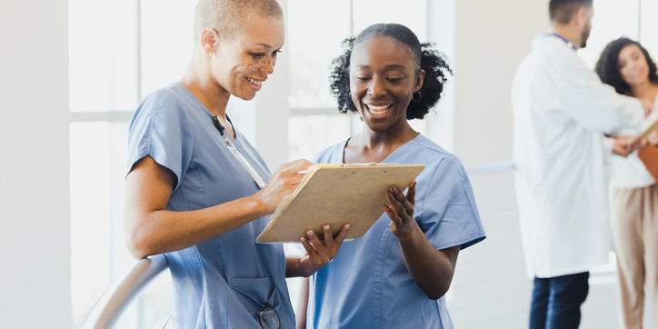 A mid adult female nurse works with a young adult female nursing student.