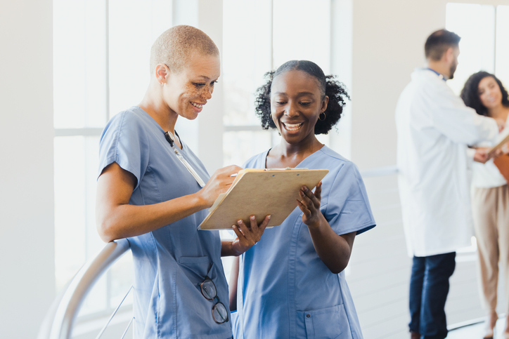 A mid adult female nurse works with a young adult female nursing student.