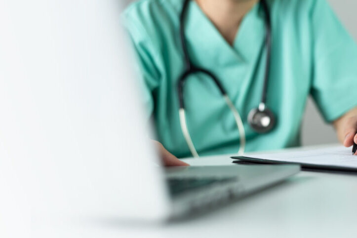 Asian female Nurse or Surgeon Doctor in green uniform working on laptop and writing something information of patient in paperwork checklist.